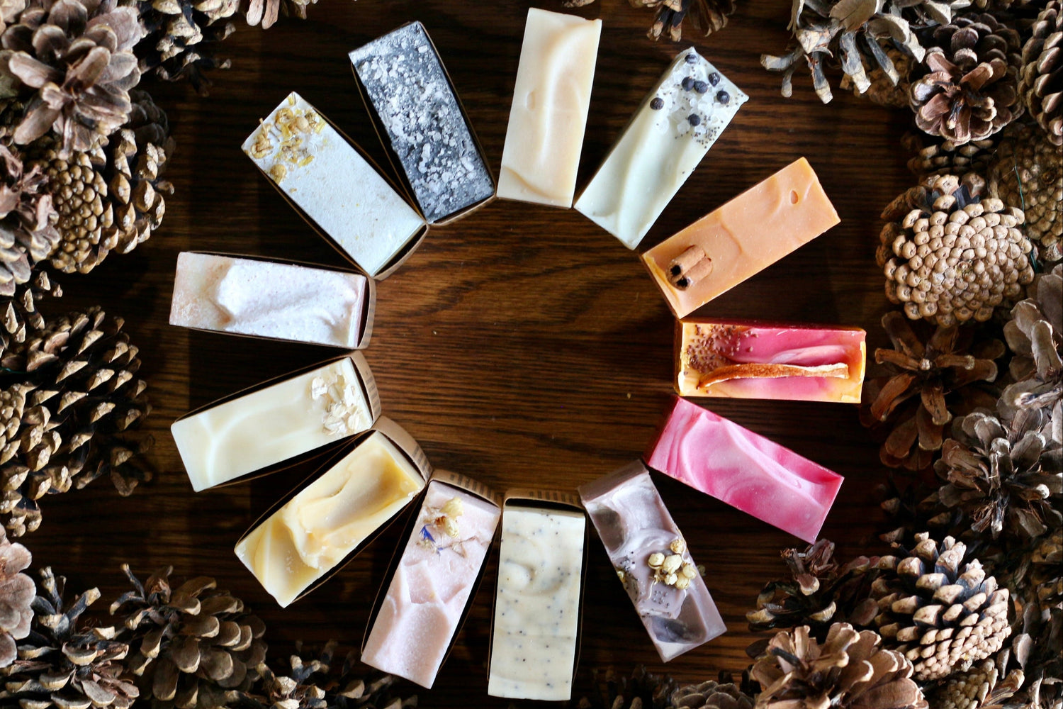 Assorted small rectangular soaps on a wooden surface surrounded by pine cones